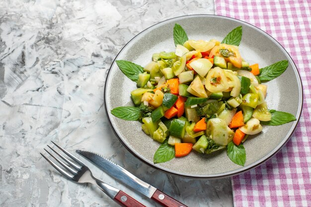 Vista inferior ensalada de tomate verde en placa ovalada un tenedor un cuchillo sobre fondo oscuro