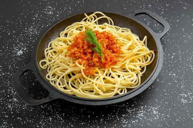 Vista inferior de espaguetis con salsa en una sartén en la mesa negra comida