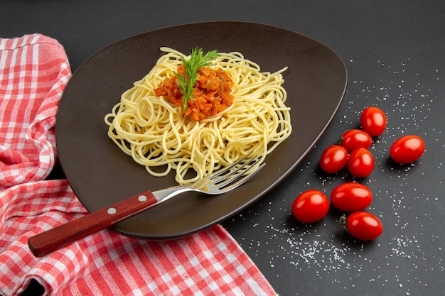 Vista inferior de espaguetis con salsa tenedor en un plato de tomates cherry, toalla de cocina a cuadros rojo blanco sobre mesa negra