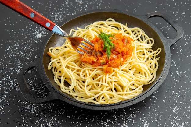 Vista inferior de espaguetis con salsa tenedor en sartén sobre mesa negra