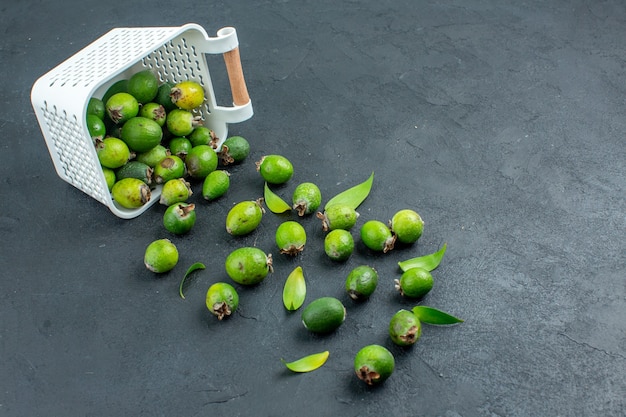 Vista inferior feijoas frescas esparcidas desde una canasta de plástico sobre una superficie oscura con espacio de copia