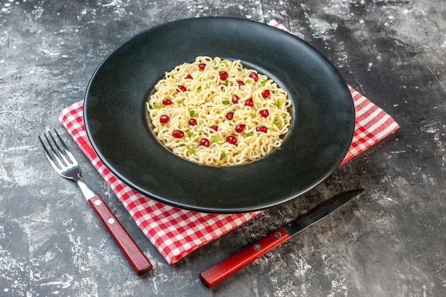 Vista inferior de fideos ramen en plato redondo oscuro servilleta a cuadros rojo blanco un tenedor y cuchillo en la mesa oscura