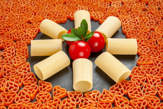 Vista inferior en forma de corazón de pasta italiana rigatoni y tomates cherry sobre una superficie oscura