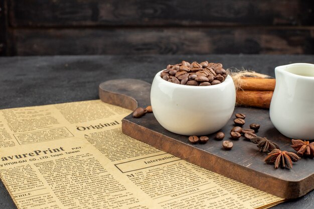 Vista inferior de los granos de café tostados en un tazón de anís palitos de canela pequeño tazón de leche en el tablero de madera en la oscuridad