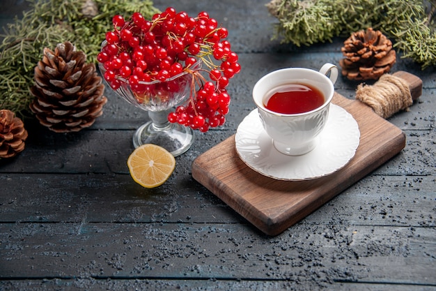 Vista inferior grosella roja en un vaso una taza de té en una tabla de cortar rodaja de piñas de limón sobre fondo de madera oscura.