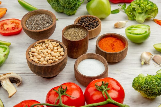 Vista inferior de guisantes de ojos negros y diferentes especias en tazones pequeños cortan verduras en la mesa gris