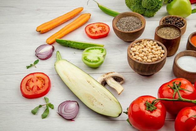 Vista inferior de guisantes de ojos negros y especias en tazones pequeños cortar verduras tomates en mesa blanca