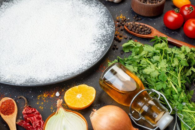 Vista inferior de harina espolvoreada en placa redonda pimienta negra en un tazón pequeño botella de aceite de tomates cebolla de cilantro en la mesa