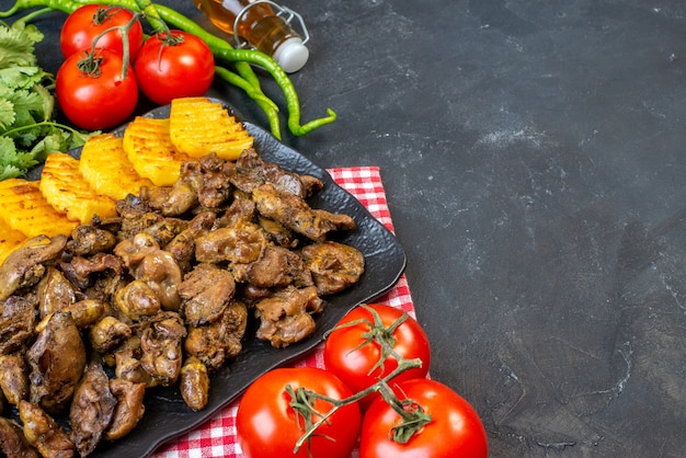 Vista inferior de hígado de pollo frito con patatas en un plato tomates pimientos verdes calientes botella de aceite de cilantro en el lugar de copia de mesa