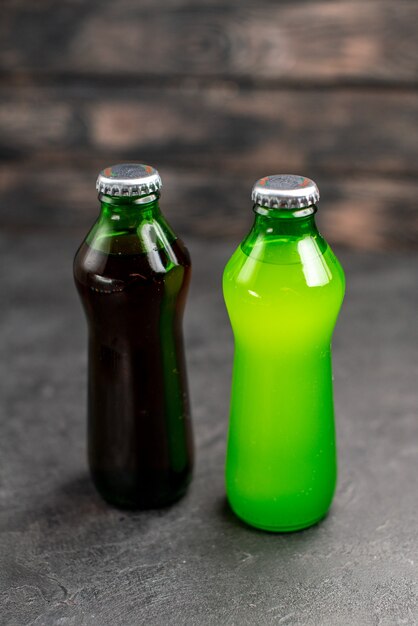 Vista inferior de limonada negra y verde en botellas sobre superficie oscura