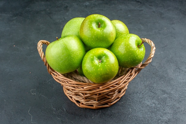 Vista inferior manzanas frescas en canasta de mimbre sobre superficie oscura