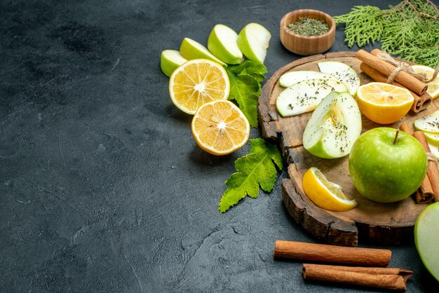 Vista inferior manzanas verdes palitos de canela rodajas de limón y manzana sobre tablero de madera polvo de menta seca en un tazón de madera en el espacio de copia de mesa negra