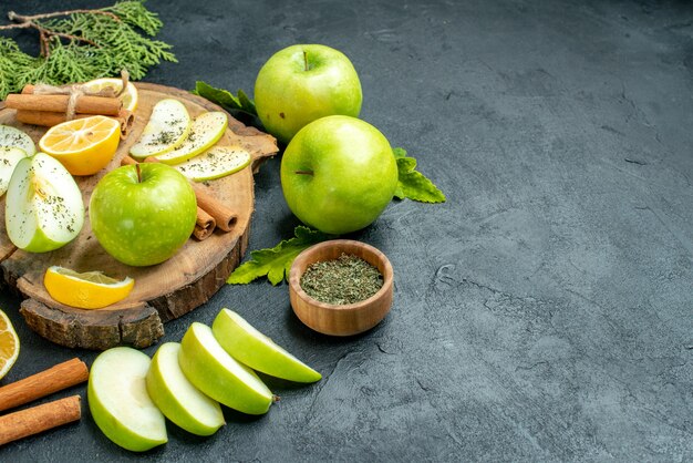 Vista inferior manzanas verdes palitos de canela y rodajas de limón rodajas de manzana sobre tablero de madera cortan limones tazón de menta seca en mesa negra espacio libre