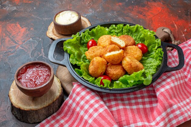 Vista inferior de nuggets de pollo en cuencos de salsa sartén sobre tablero de madera mantel rojo sobre fondo rojo oscuro