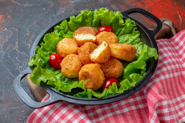 Vista inferior de nuggets de pollo lechuga tomates cherry en sartén sobre fondo rojo oscuro