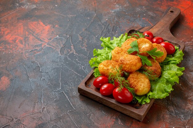 Vista inferior nuggets de pollo lechuga tomates cherry sobre tablero de madera sobre mesa oscura