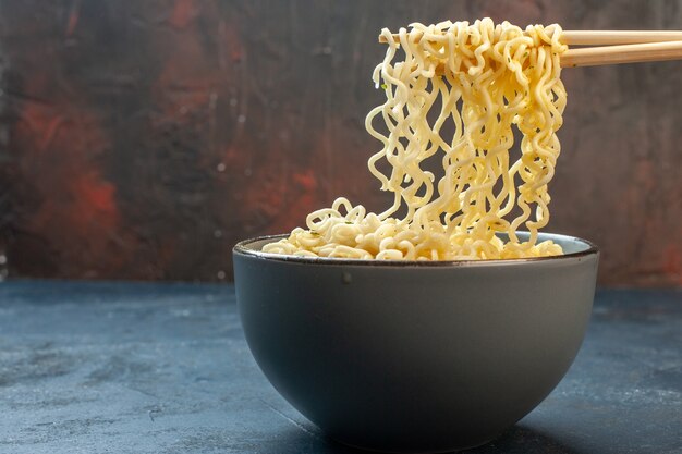 Vista inferior de los palillos de fideos ramen asiáticos en un tazón en la mesa oscura waribashi