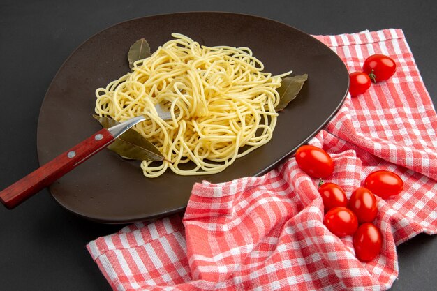 Vista inferior de pasta de espagueti con hojas de laurel tenedor en plato tomates cherry toalla de cocina a cuadros rojos y blancos sobre mesa negra