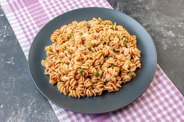 Vista inferior de la pasta rotini en un plato redondo sobre un mantel a cuadros blanco rosa sobre una superficie oscura