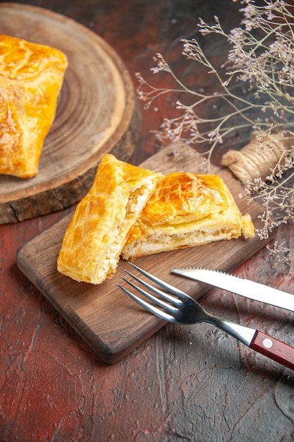 Foto gratuita vista inferior penovani khachapuri sobre tablero de madera y sobre tabla de cortar cuchillo y tenedor sobre mesa rojo oscuro