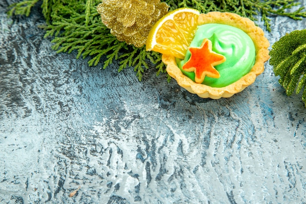 Vista inferior pequeña tarta con ramas de pino de crema pastelera verde en el espacio libre de la superficie gris