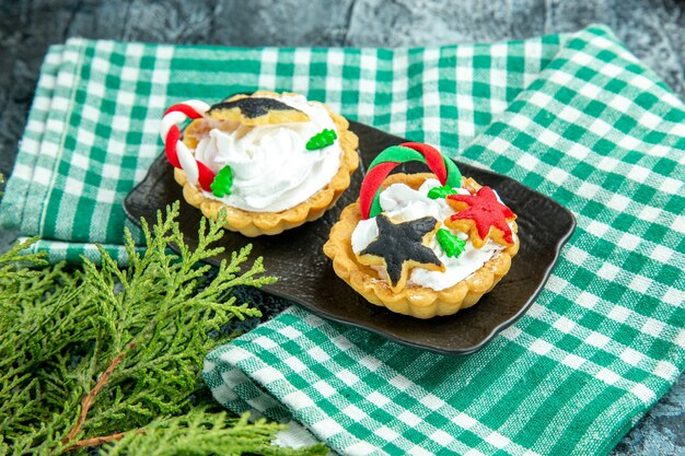 Vista inferior de las pequeñas tartas de Navidad en la placa negra sobre el mantel de mesa gris