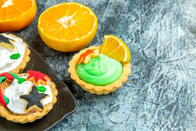 Vista inferior pequeñas tartas navideñas en placa negra cortadas naranjas en mesa gris