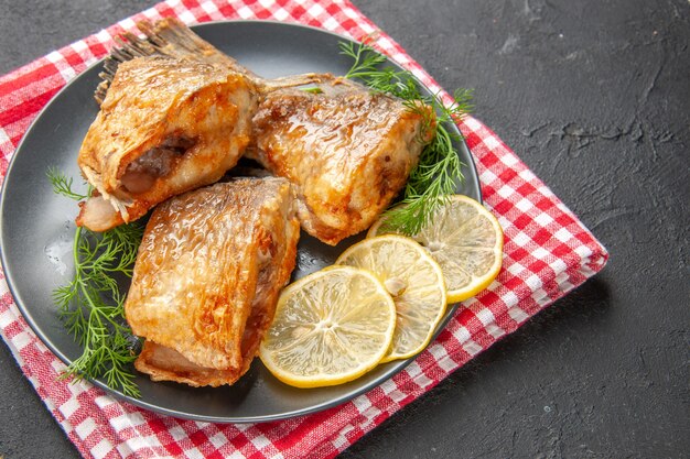 Vista inferior de pescado frito con rodajas de limón en un plato sobre una servilleta sobre fondo negro