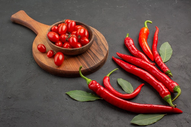 Vista inferior de pimientos rojos y hojas de pago y un tazón de tomates cherry en la tabla de cortar en el cuadro negro