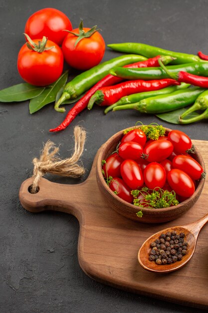 Vista inferior pimientos rojos y verdes calientes y la bahía de tomates deja un tazón con tomates cherry y pimienta negra en una cuchara sobre una tabla de cortar sobre suelo negro