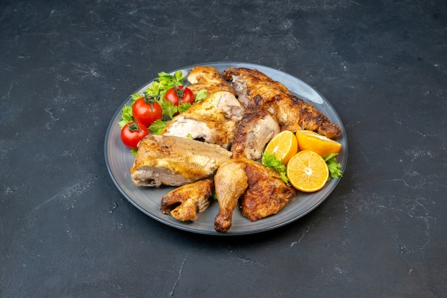 Vista inferior de pollo asado con tomates frescos rodajas de limón en la placa sobre la mesa negra
