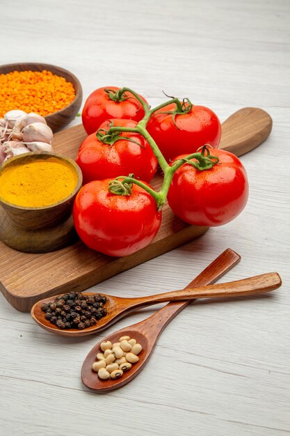 Vista inferior de la rama de tomate fresco ajo cúrcuma en una tabla de cortar cucharas de madera con pimienta negra y frijoles en la mesa gris