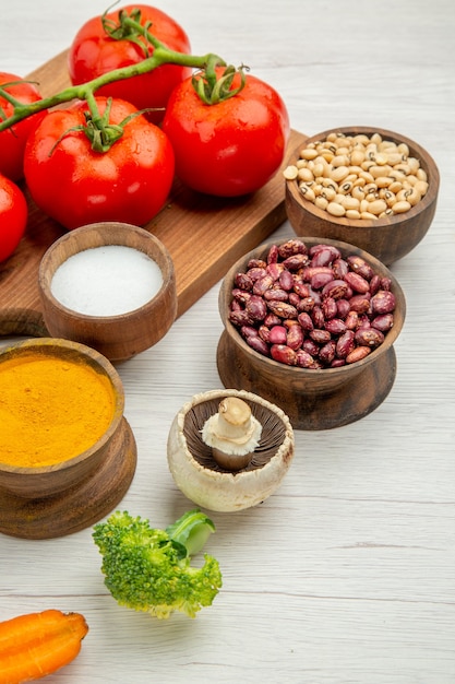 Vista inferior de la rama de tomate en la tabla de cortar, sal, cúrcuma, champiñones, brócoli, cuencos de frijoles en la mesa