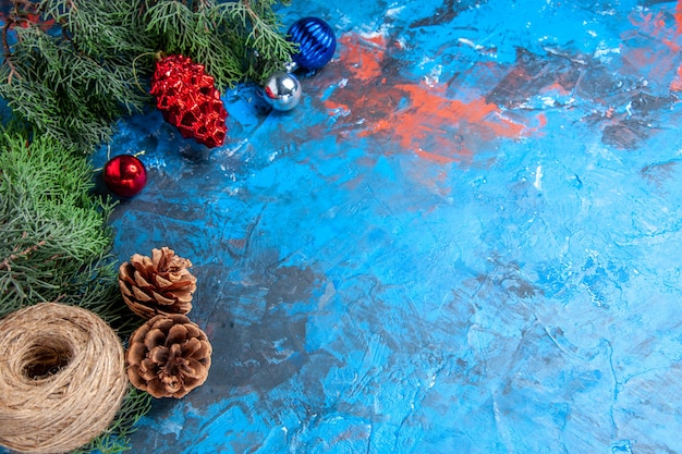 Foto gratuita vista inferior de las ramas de los árboles de pino con piñas y coloridos juguetes de árbol de navidad hilo de paja sobre fondo azul-rojo con espacio libre