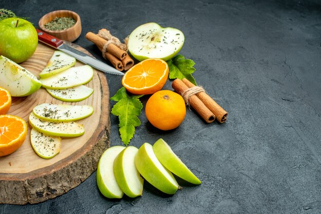 Vista inferior rebanadas de manzana y mandarina cuchillo sobre tablero de madera palitos de canela atados con cuerda de menta seca en polvo en el espacio libre de la mesa negra