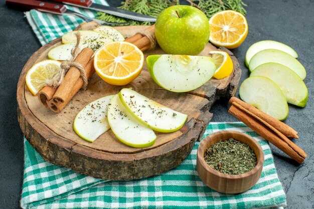 Vista inferior rebanadas de manzana palitos de canela y rodajas de limón manzana sobre tablero de madera un tenedor y cuchillo sobre una servilleta verde sobre fondo negro