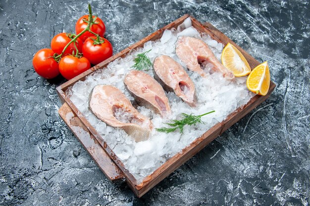 Vista inferior rebanadas de pescado crudo con hielo en la rama de tomate de tablero de madera en la mesa