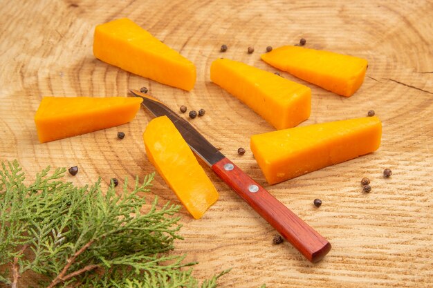 Vista inferior rebanadas de queso espolvoreado pimienta negra cuchillo rama de pino sobre mesa de madera