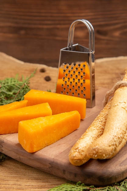 Vista inferior de las rebanadas de queso rallador de pan en la tabla de cortar las ramas de los árboles de pino en la mesa de madera