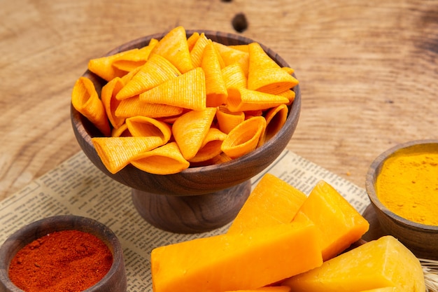 Vista inferior rebanadas de queso en un tazón de pimiento rojo en polvo chips espiga de trigo en el periódico en la mesa aislada