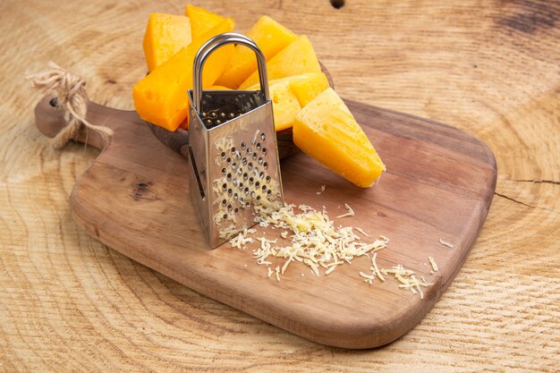 Vista inferior de las rebanadas de queso en un tazón rallador de caja en la tabla de cortar sobre la superficie de madera