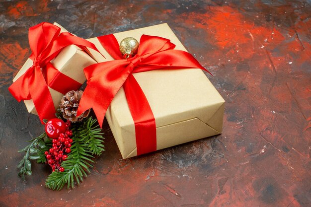 Vista inferior de regalos de Navidad atados con cinta roja rama de árbol de Navidad en la mesa de color rojo oscuro