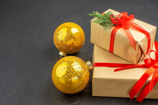 Vista inferior de regalos de Navidad grandes y pequeños en papel marrón atados con bolas de Navidad de cinta roja en la oscuridad