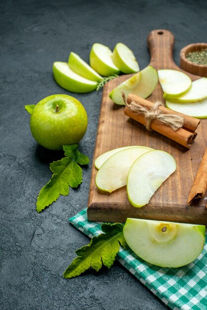 Vista inferior de rodajas de manzana y canela en una tabla de cortar polvo de menta seca en un tazón mantel verde manzana sobre una mesa oscura