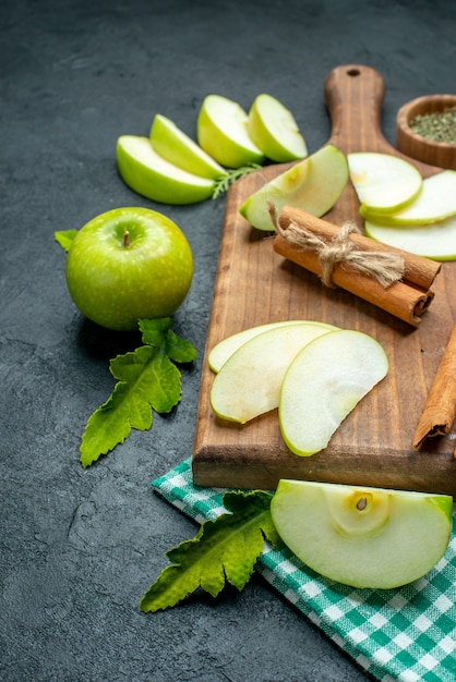 Vista inferior de rodajas de manzana y canela en una tabla de cortar polvo de menta seca en un tazón mantel verde manzana sobre una mesa oscura