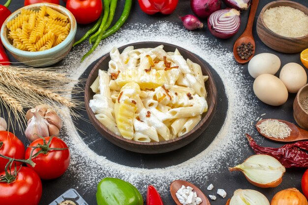 Vista inferior de la sabrosa pasta penne en un tazón, tomates, pasta espiral cruda y arroz en tazones, huevos en la mesa