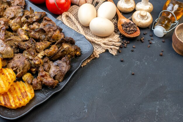 Vista inferior sabroso kebab con patatas en plato huevos champiñones pimienta negra en cuchara de madera botella de aceite de tomates en lugar de copia de mesa oscura