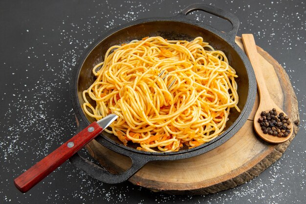 Vista inferior sartén de espaguetis pimienta negra en cuchara de madera sobre tablero de madera sobre fondo oscuro