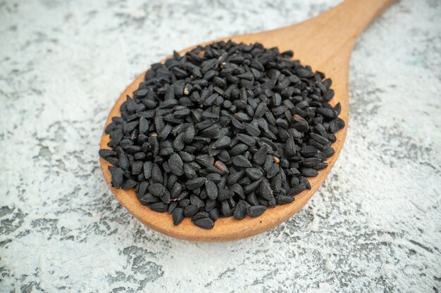 Vista inferior de semillas de comino negro en cuchara de madera sobre gris