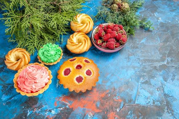 Foto gratuita vista inferior tarta de frambuesa tartas pequeñas galletas tazón con frambuesas en el espacio de copia de mesa azul